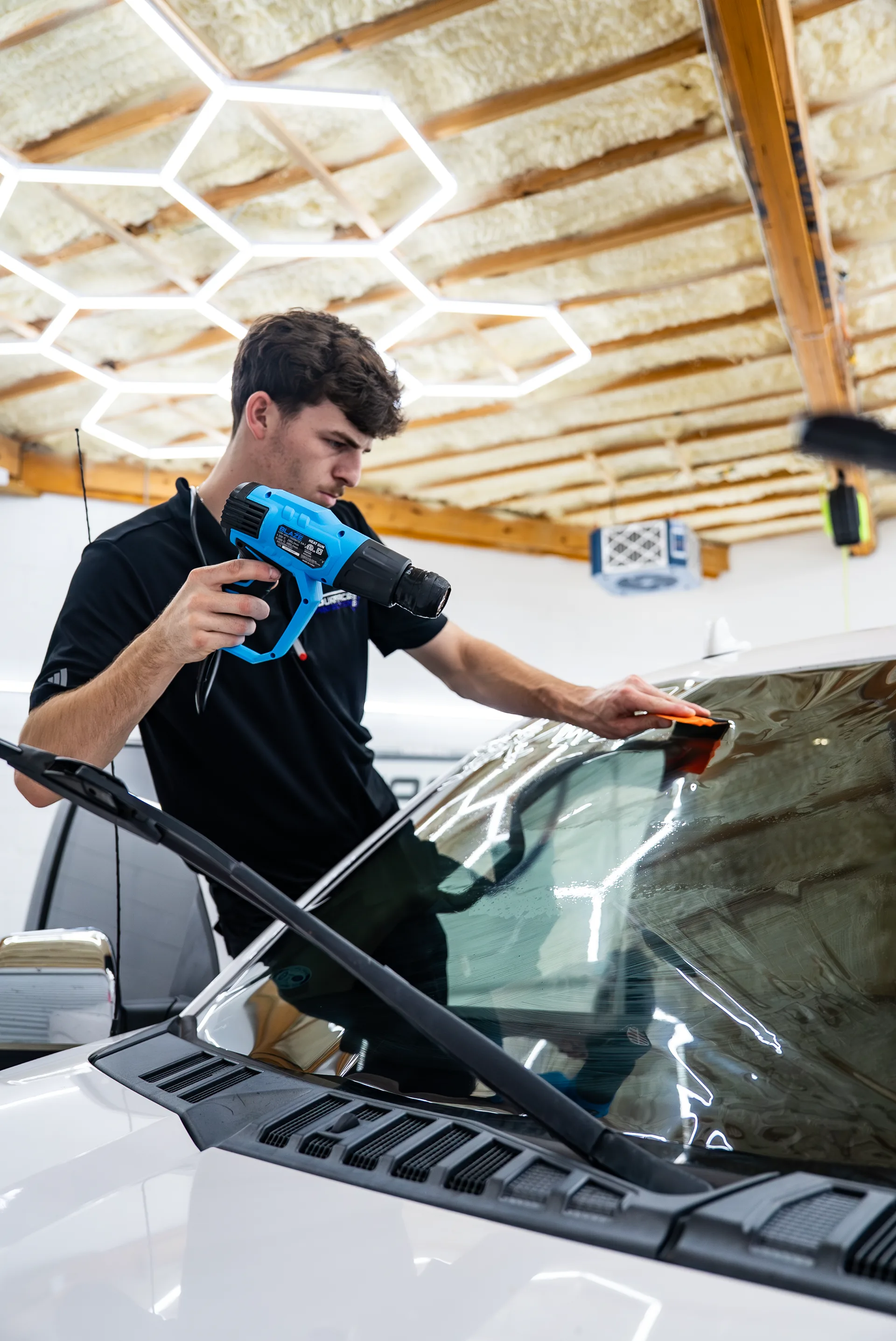 Technician working a heat gun along a vehicle's side glass
